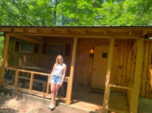 Brooke B stands next to one of the camp cabins at Camp Walden. She offers support through summer programs for teens in West Bloomfield, MI. Learn more about camps for teens, and how summer programs for teens can help them thrive!
