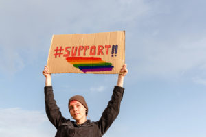 A woman holds a sign above their head with the word "#support!!" This could represent LGBTQ youth support in West Bloomfield, MI. Contact the Rainbow Group for support for LGBTQ youth. We would be honored to support you!