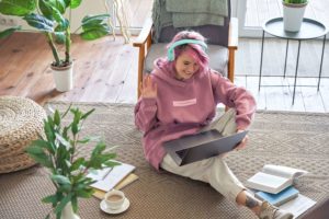 A woman waves at her laptop as she starts a video call. Therpayology can offer support from the comfort of home with group therapy in West Bloomfield, MI. Contact us to learn more about trauma group therapy and group therapy for teens in San Fransisco, CA. | 48322 | 94118 | 48324