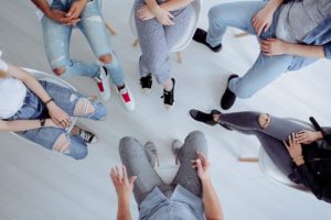 A top down view of a group of people sitting and talking in a circle. This represents the support group therapy in West Bloomfield, MI can offer. Learn more about group therapy in San Francisco, CA, and the services we offer including group therapy for teens, group therapy for trauma, and more! | 48322 | 94118 | 48324